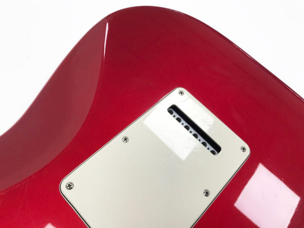 Close-up of red electric guitar back showing white tremolo cavity cover plate with screws and string tension spring slot