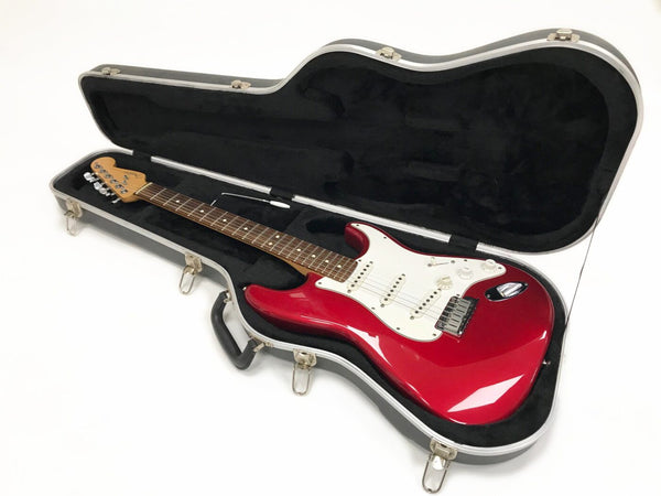 Red electric guitar with white pickguard and rosewood fretboard in black hard case with plush interior, displayed on white background