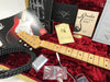 Fender Stratocaster guitar neck with tuning pegs inside red velvet guitar case with Fender custom shop documents, tremolo arm, guitar cable, and care guides