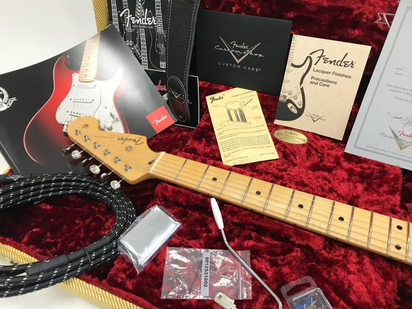 Fender Stratocaster guitar neck with tuning pegs inside red velvet guitar case with Fender custom shop documents, tremolo arm, guitar cable, and care guides