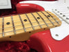 Close-up of maple fretboard with metal frets and dot inlays on red electric guitar body with white pickguard resting on red plush interior
