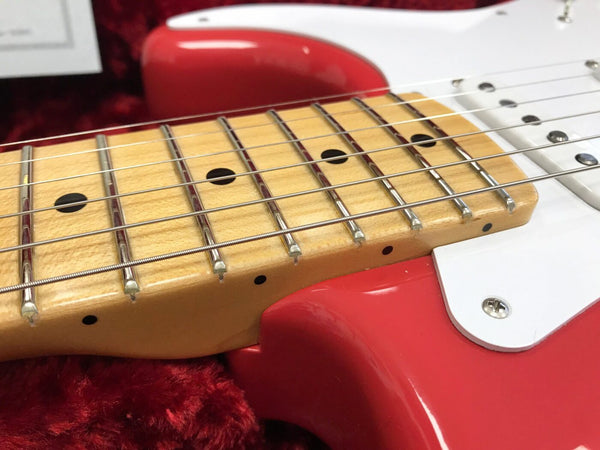 Close-up of maple fretboard with metal frets and dot inlays on red electric guitar body with white pickguard resting on red plush interior