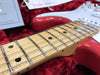 Close-up of maple fretboard and strings on red electric guitar in red velvet-lined case with Fender tag in background