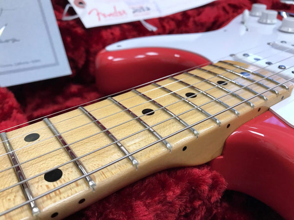 Close-up of maple fretboard and strings on red electric guitar in red velvet-lined case with Fender tag in background