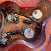 Close-up of vintage electric guitar control cavity showing aged potentiometers, capacitors, and wiring on wooden body with red finish.