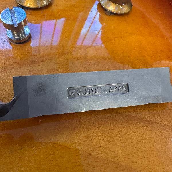 Close-up of Gotoh Japan guitar bridge part on a sunburst electric guitar body with volume and tone control knobs visible.