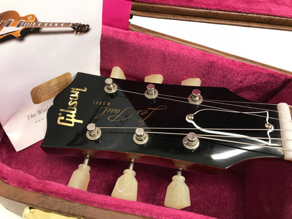 Close-up of Gibson Les Paul guitar headstock with tuning pegs inside pink velvet-lined hard case with Gibson certificate booklet.