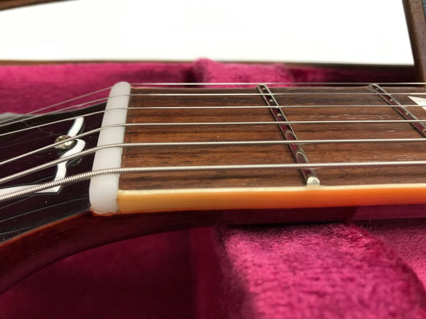 Close-up view of electric guitar fretboard showing metal strings, nut, and inlays, resting on a plush red guitar case lining