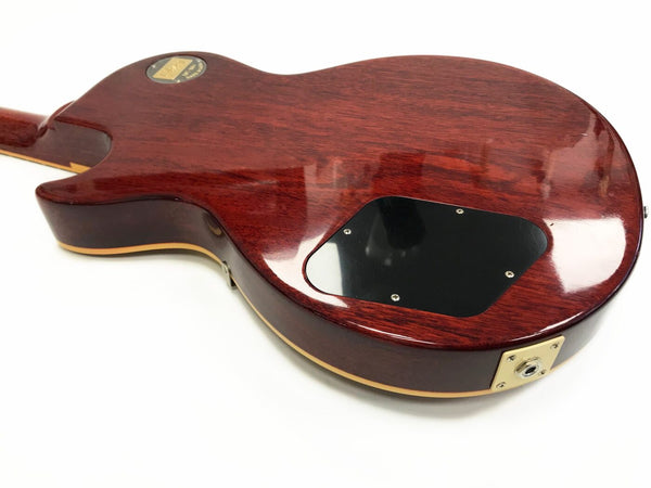 Back view of a glossy mahogany electric guitar body with cream binding, black plastic control cavity cover, and gold output jack plate on white background