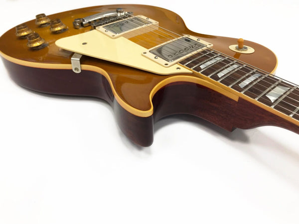 Close-up of honey burst electric guitar body and neck showing chrome pickups, cream pickguard, and control knobs on white background