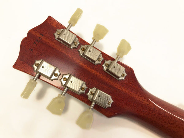 Close-up of vintage guitar headstock tuners with cream-colored tuning pegs on a reddish-brown wooden guitar neck.