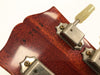 Close-up of vintage guitar headstock with serial number 87283 and metal tuning pegs with cream-colored tuning keys on reddish-brown wood finish