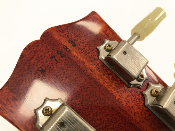Close-up of vintage guitar headstock with serial number 87283 and metal tuning pegs with cream-colored tuning keys on reddish-brown wood finish