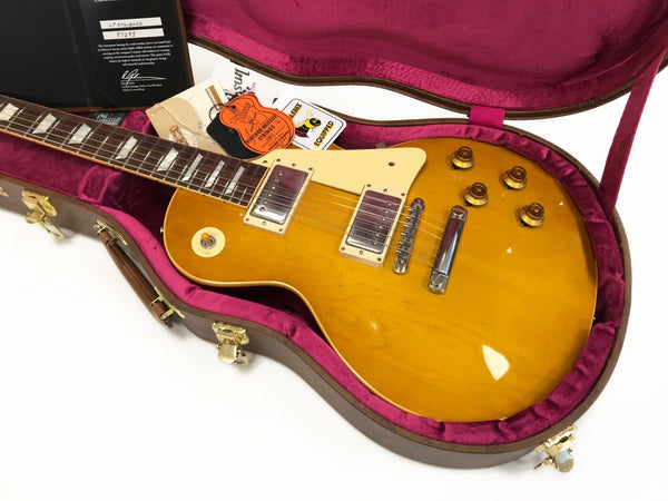 Gibson Les Paul Standard electric guitar in honey burst finish with cream pickguard, humbucker pickups, and brass control knobs inside a pink plush-lined hard case with tags and certificate