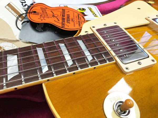 Close-up of honey burst electric guitar neck and pickup with vintage Gibson strings tag and treble switch knob on wooden guitar body