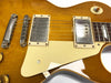 Close-up of honey burst electric guitar body showing chrome humbucker pickups, cream pickguard, bridge, and tone selector switch labeled Rhythm and Treble