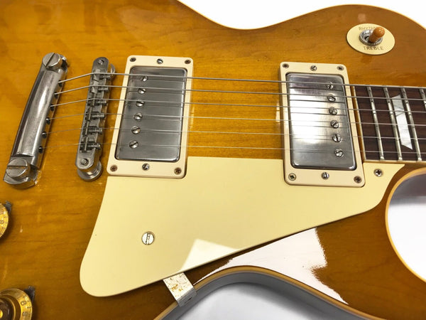 Close-up of honey burst electric guitar body showing chrome humbucker pickups, cream pickguard, bridge, and tone selector switch labeled Rhythm and Treble