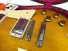 Close-up of honey burst electric guitar body showing bridge, pickup, and control knobs in plush purple guitar case with vintage tags