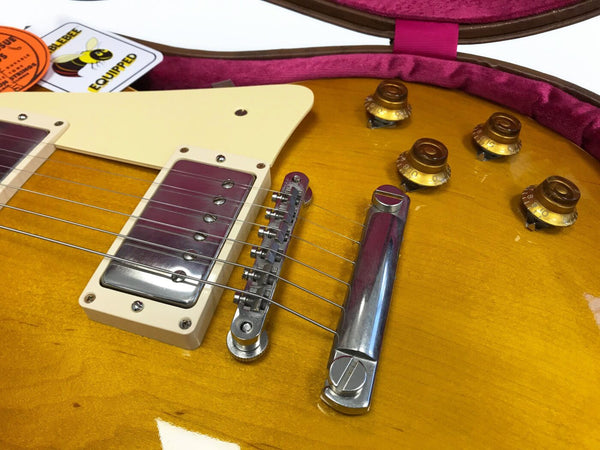 Close-up of honey burst electric guitar body showing bridge, pickup, and control knobs in plush purple guitar case with vintage tags