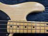 Close-up of natural wood electric bass guitar body and fretboard with metal frets and black dot inlays on dark fabric background