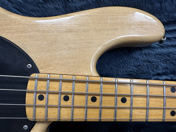 Close-up of natural wood electric bass guitar body and fretboard with metal frets and black dot inlays on dark fabric background