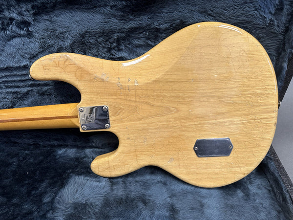 Vintage natural finish electric guitar body showing wood grain and wear, resting on dark gray plush guitar case lining