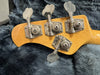 Close-up of vintage Music Man bass guitar tuning pegs on natural wood headstock resting on plush gray fabric background
