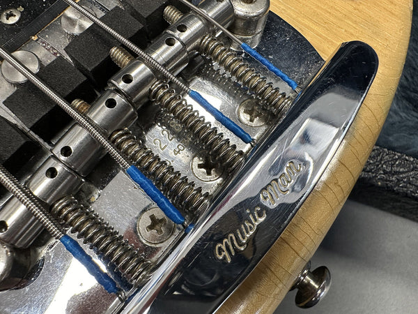 Close-up of Music Man electric guitar bridge with steel strings and chrome hardware on natural wood finish body