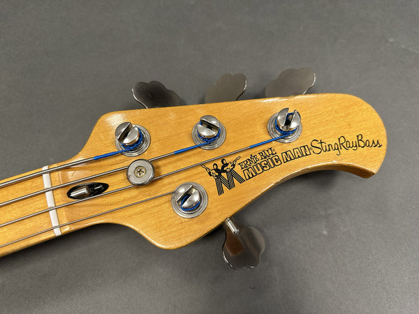 Close-up of Ernie Ball Music Man StingRay Bass guitar headstock with tuning pegs and strings on gray background