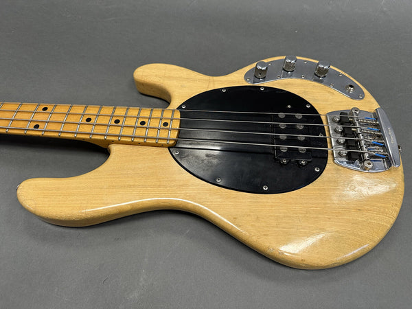 Natural finish electric bass guitar with maple neck, black pickguard, and chrome control knobs and bridge on gray background