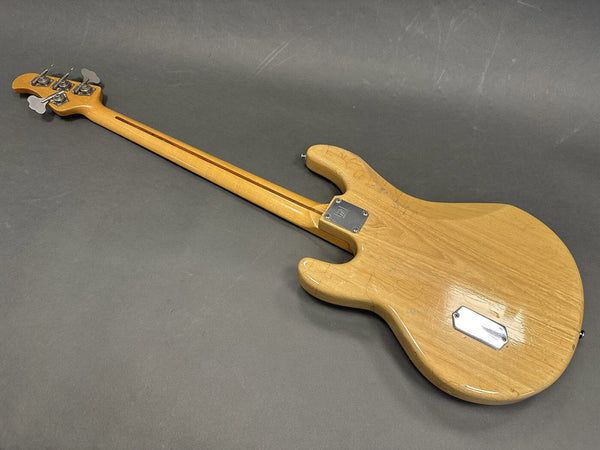 Back view of natural wood electric bass guitar with chrome hardware on gray background