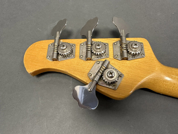 Close-up of natural wood bass guitar headstock with four silver tuning pegs and gear mechanisms on gray background