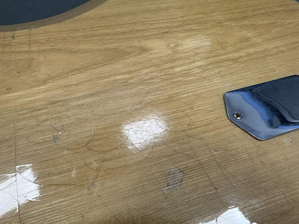Close-up of worn light wood guitar body with scratches and chipped finish near chrome control plate screw