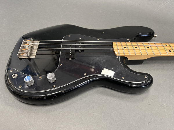 Black electric bass guitar with maple neck and two control knobs on gray background