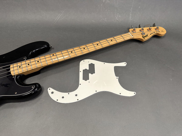 Black Greco Mercury Bass guitar with maple neck and frets next to a white pickguard on gray background