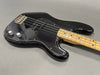 Black electric bass guitar with maple neck and chrome hardware on gray background, close-up of body and fretboard