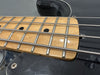 Close-up of electric bass guitar fretboard with steel strings and black body showing maple wood neck and fret markers