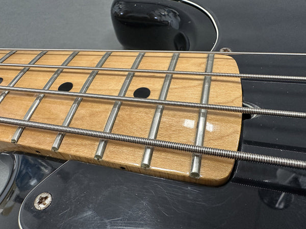 Close-up of electric bass guitar fretboard with steel strings and black body showing maple wood neck and fret markers
