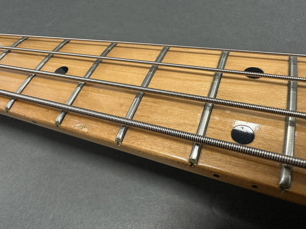 Close-up of maple guitar neck fretboard with four metal strings and black dot inlays on a gray background