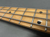 Close-up of maple guitar fretboard with metal frets, black dot inlays, and wound strings on dark background