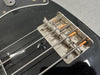 Close-up of vintage electric bass guitar bridge with metal saddles and wound steel strings on black body