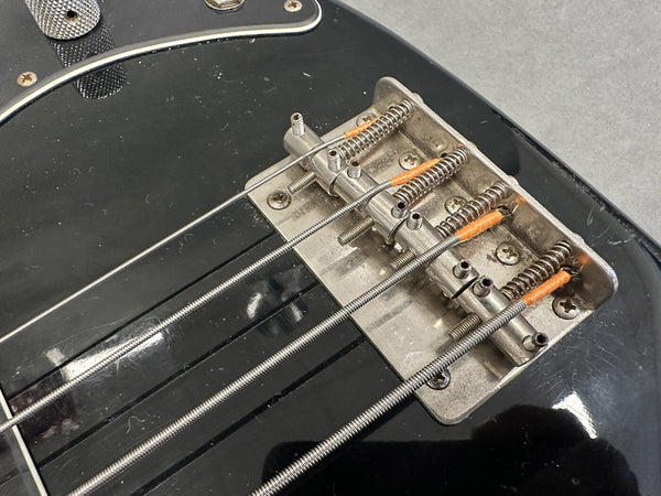 Close-up of vintage electric bass guitar bridge with metal saddles and wound steel strings on black body