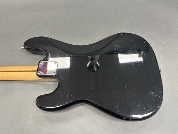 Back of black electric guitar body with visible scratches and dents, maple neck with dual stripe, metal neck plate on gray background