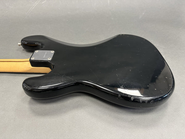 Black electric guitar body back with visible scratches and wear, maple neck with four-bolt neck plate on gray background