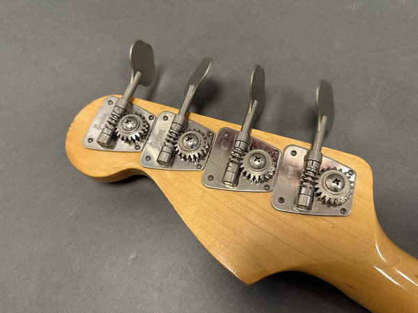 Close-up of four metal tuning pegs on natural wood headstock of bass guitar against gray background
