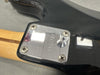 Close-up of electric guitar neck plate with serial number E801721 on black guitar body and wooden neck, showing screw details and wood grain quality.