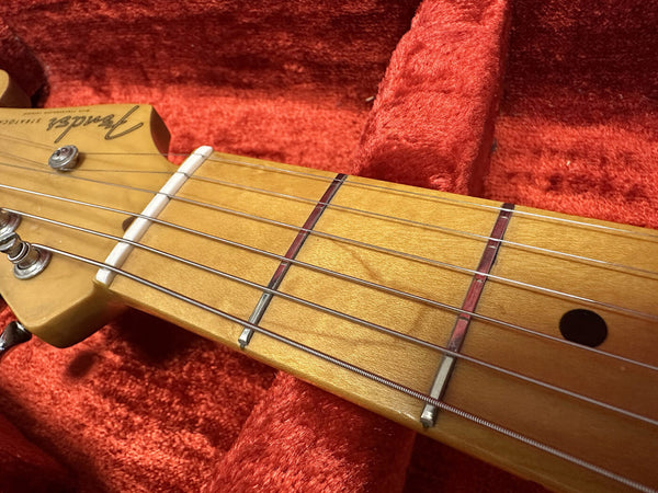 Close-up of Fender Stratocaster maple guitar neck and fretboard with metal frets and strings on red plush guitar case interior