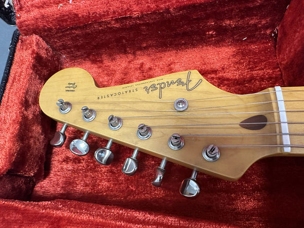 Close-up of Fender Stratocaster guitar headstock with tuning pegs, maple neck, and original decal in red velvet guitar case