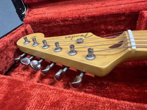 Close-up of Fender Stratocaster guitar headstock with tuning pegs inside red velvet-lined hard case