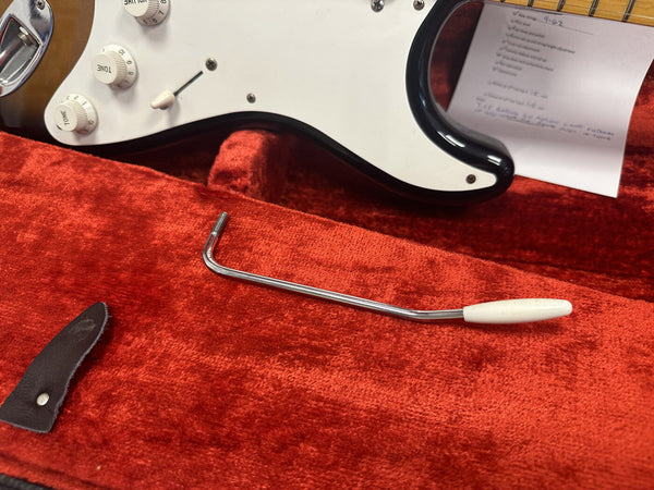 Close-up of white pickguard and tone knobs on electric guitar with tremolo arm lying on red velvet guitar case lining